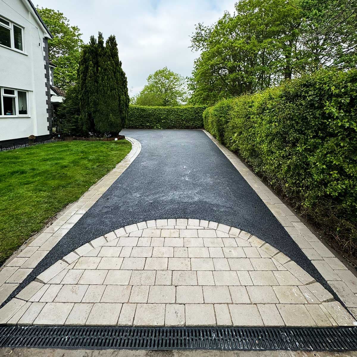 Long freshly finished black driveway with a pale block-paved crescent and green hedges